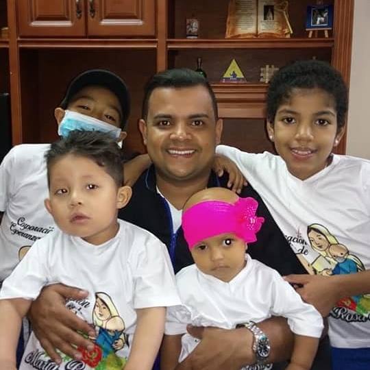 Hombre con cuatro hijos, sonriendo, algunos con camisas iguales. Interior, con un armario de madera al fondo.