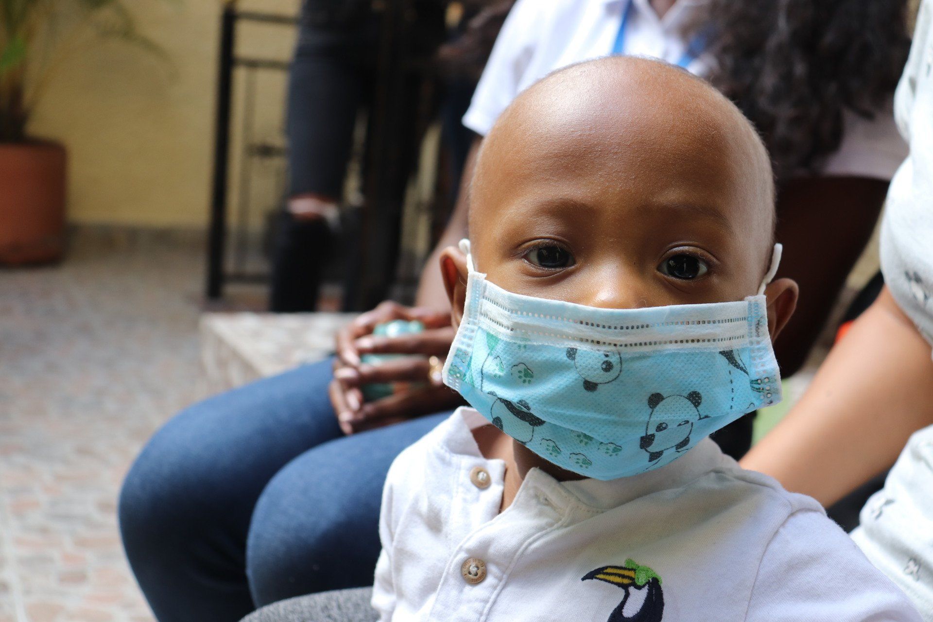 Niño con mascarilla, mirando a la cámara. Está frente a un fondo borroso.
