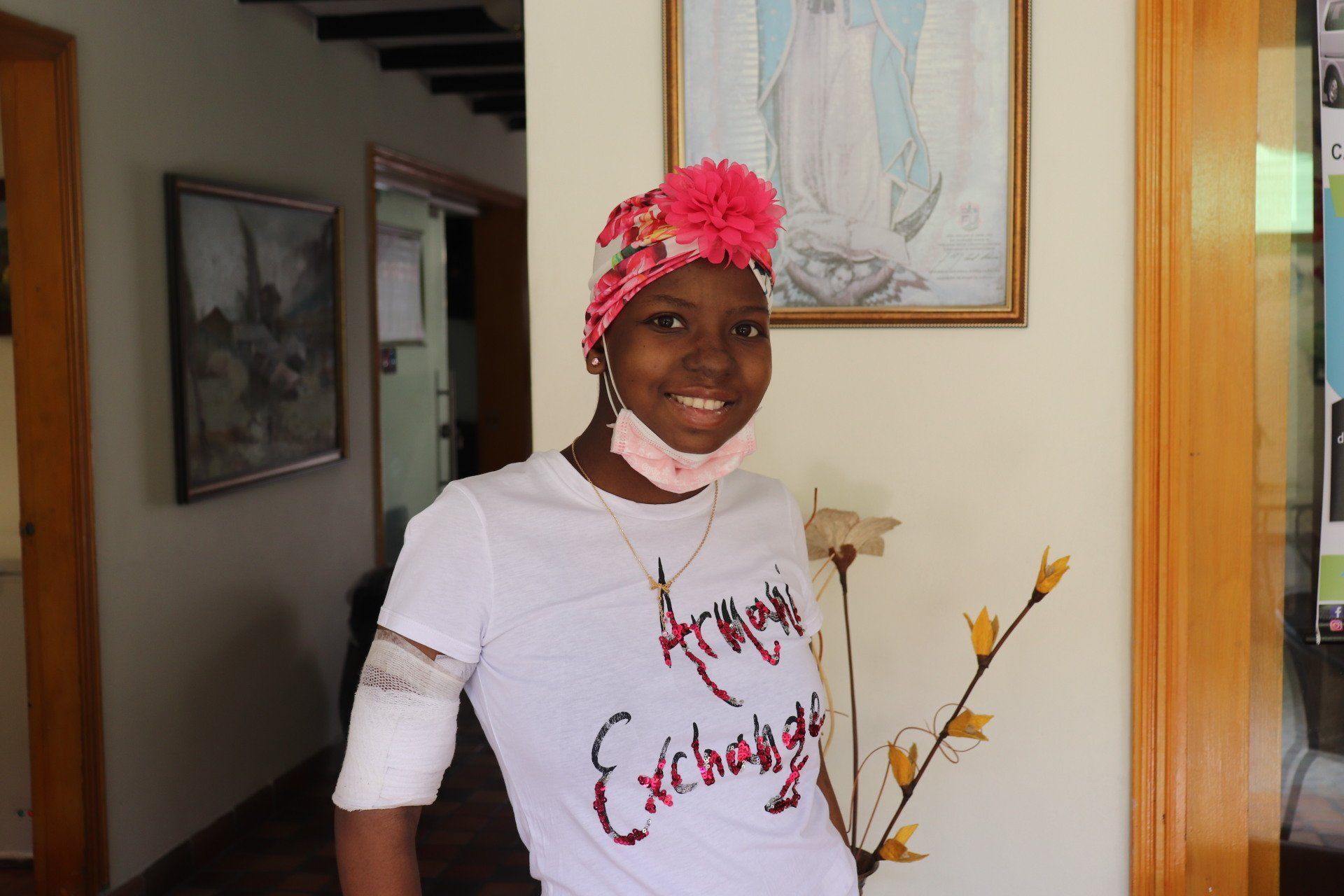Una persona sonriente, con una camiseta blanca y un pañuelo rosa en la cabeza y un brazo enyesado