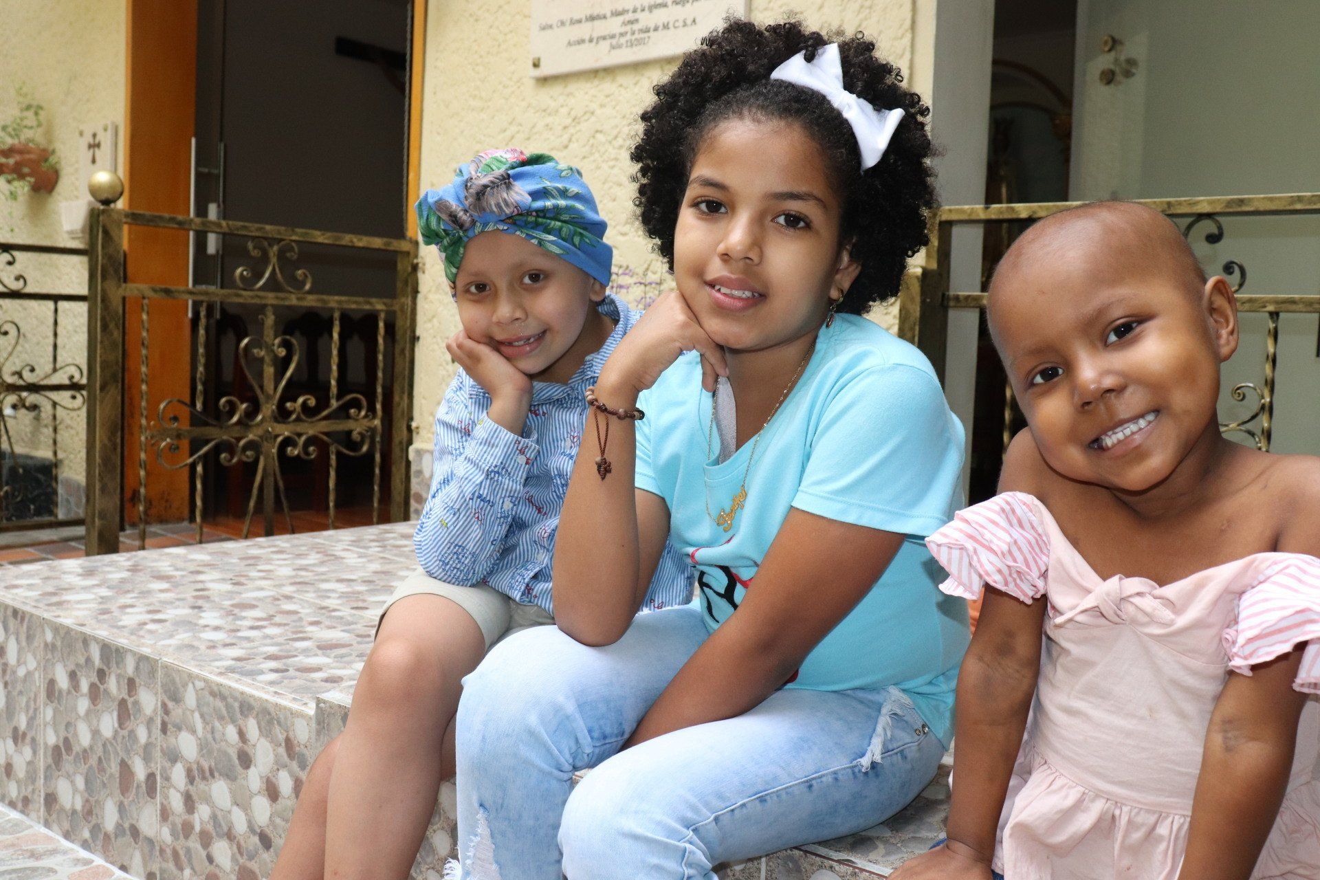 Tres jóvenes sentadas en unas escaleras, sonriendo a la cámara. Una con el pelo rizado y un lazo