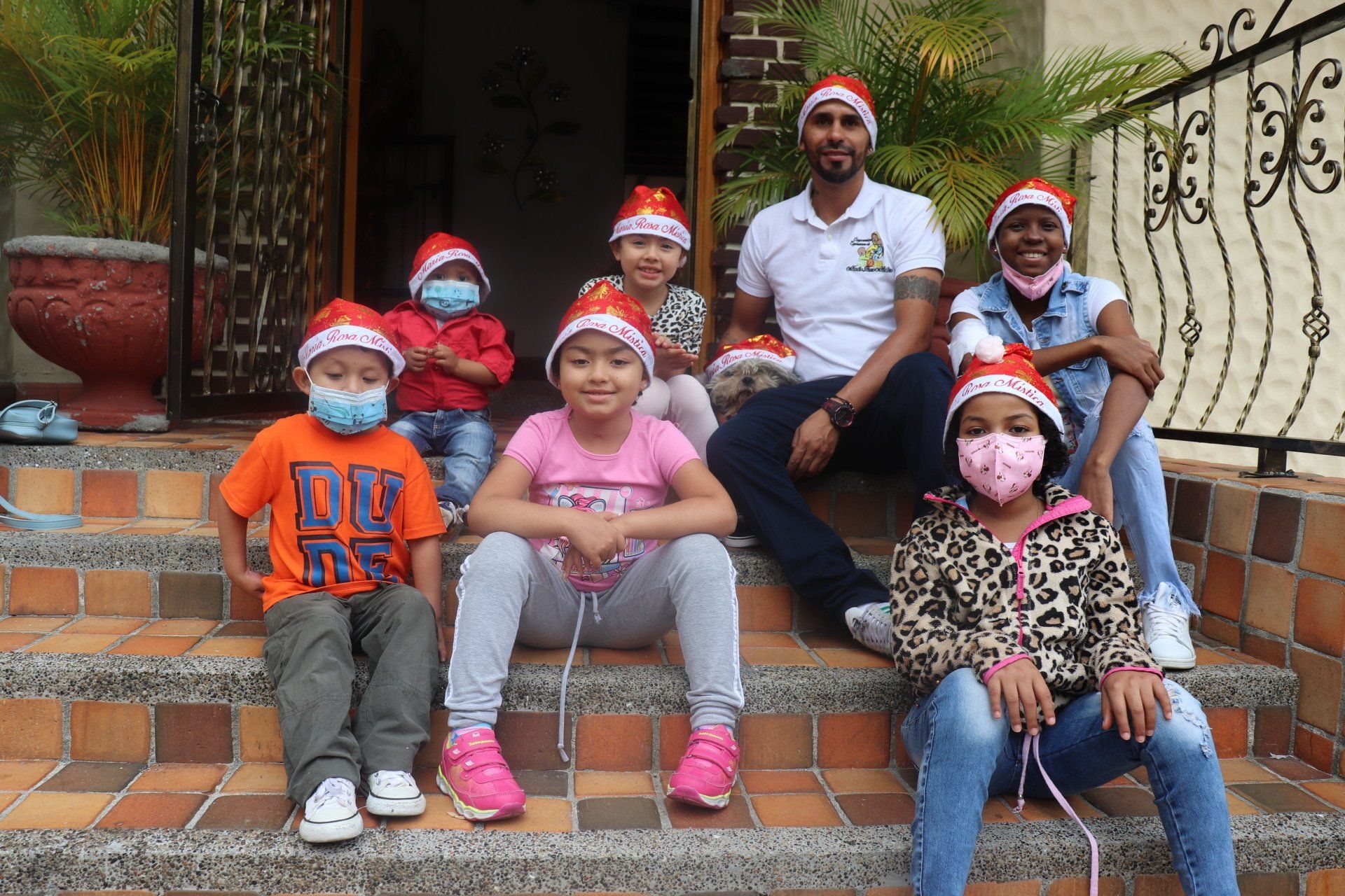Grupo de personas con gorros de Papá Noel en las escaleras. Algunos llevan mascarillas. Edificio al fondo.