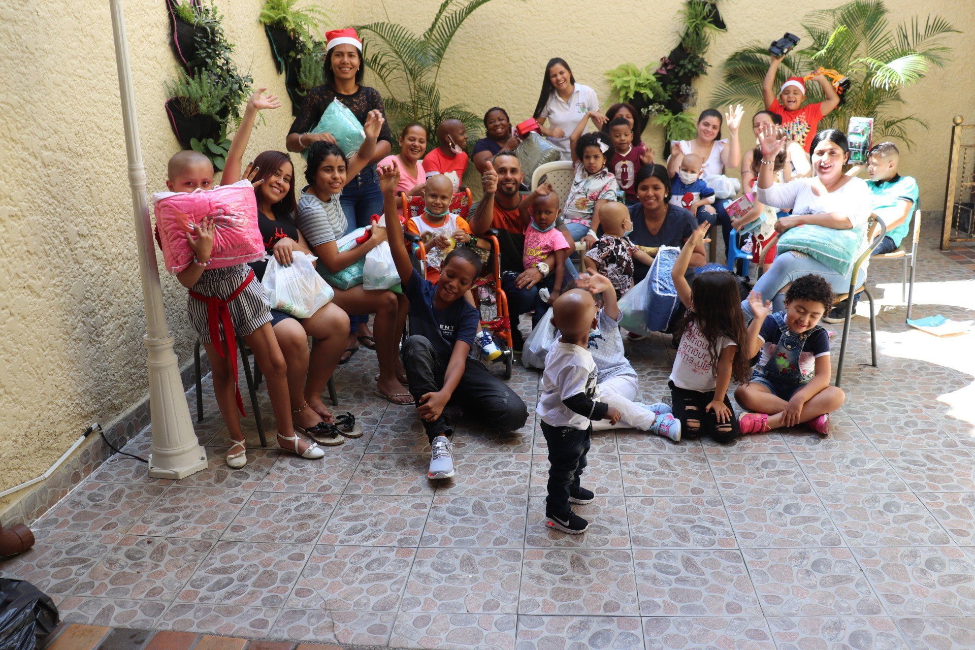 Un grupo de personas, incluyendo niños, saludando afuera. Algunos sostienen regalos, sonriendo.