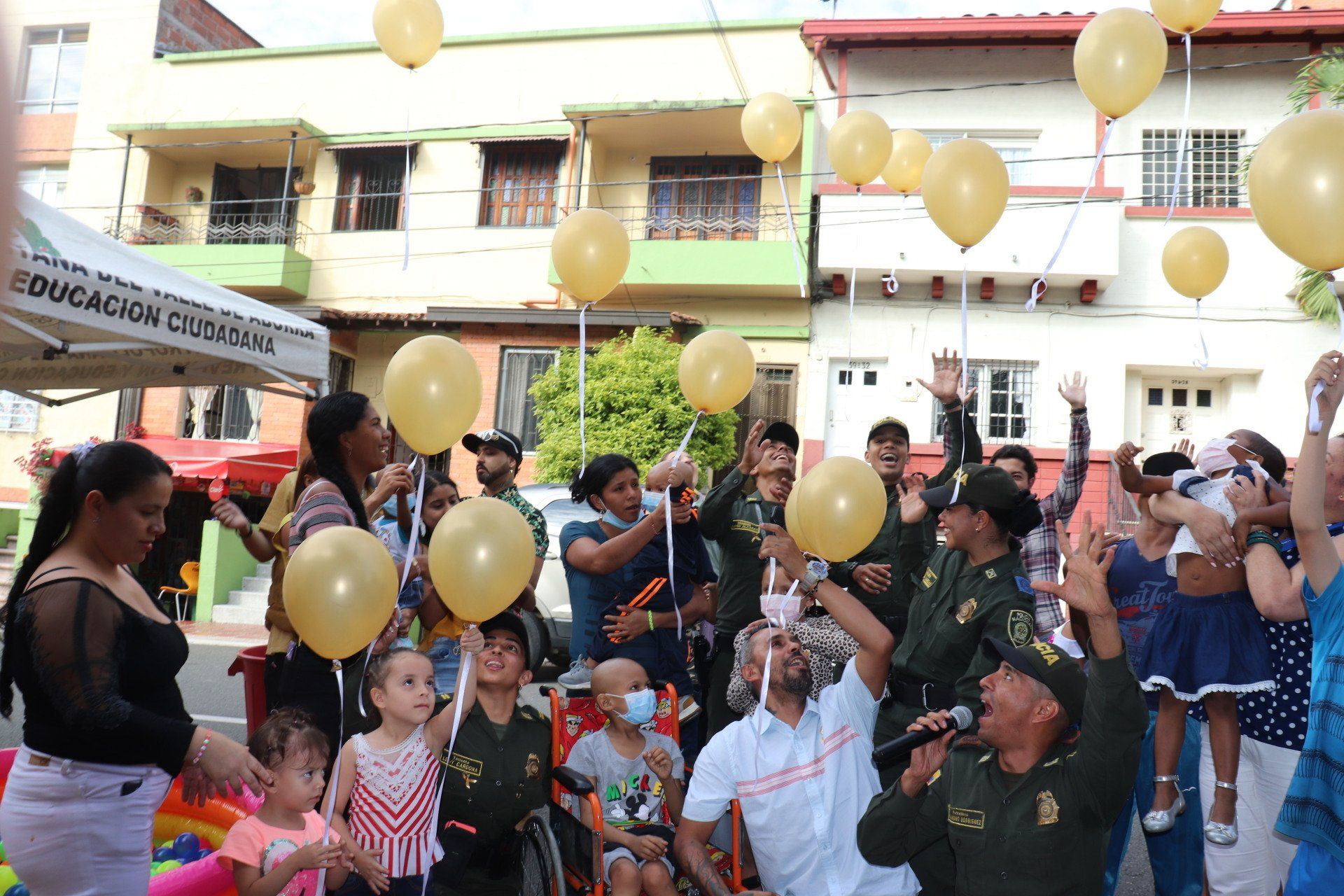 Personas, incluida la policía, lanzando globos amarillos en un evento comunitario al aire libre.