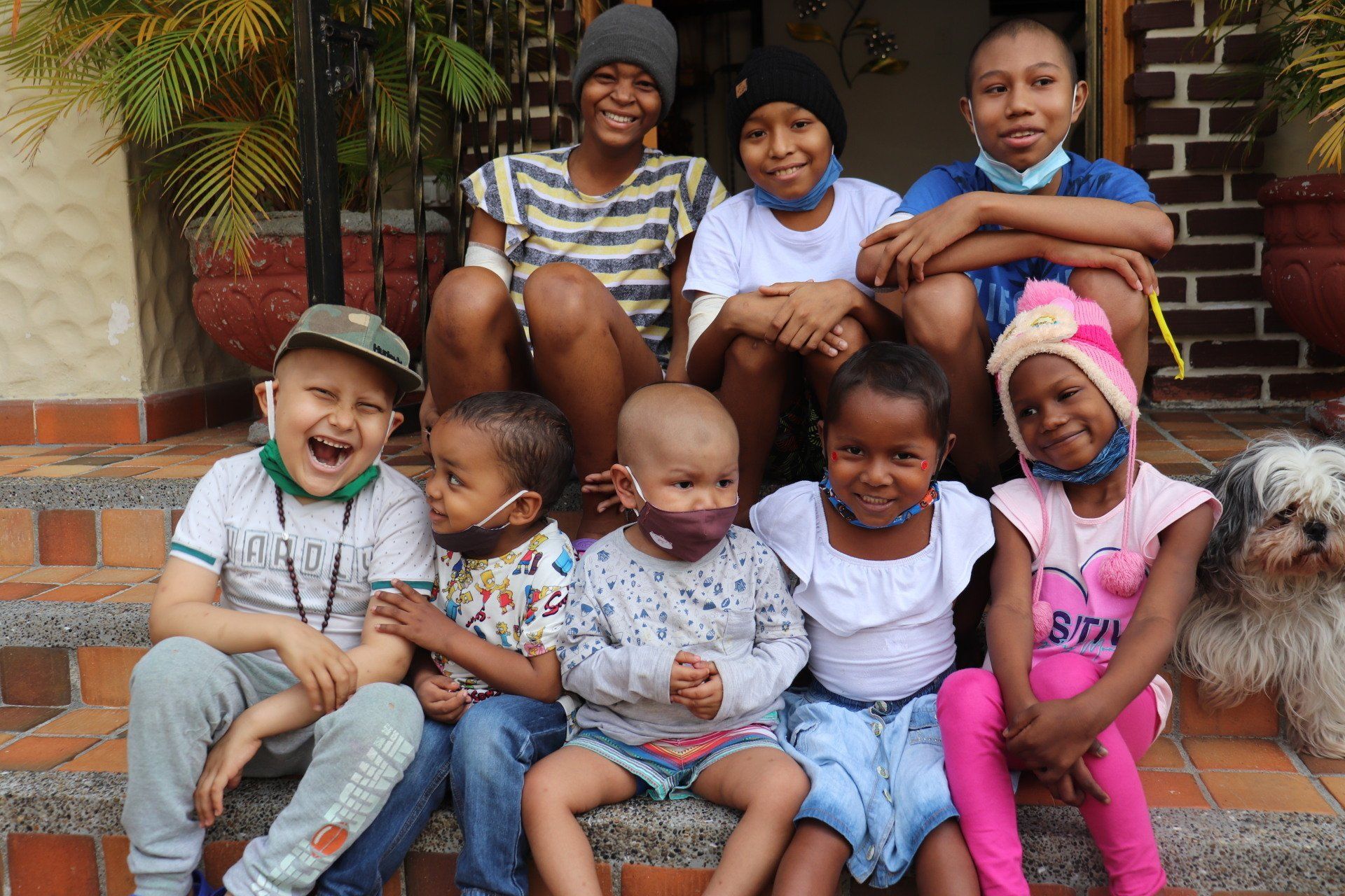 Grupo de niños sonriendo y posando en las escaleras afuera de un edificio; algunos llevan máscaras y sombreros.