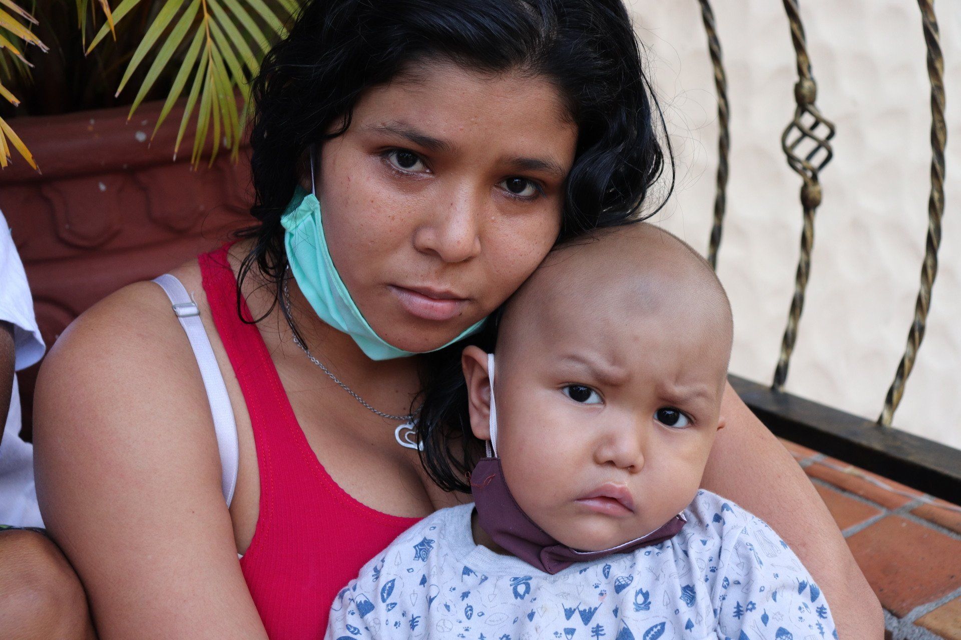 Una mujer con una camiseta roja sostiene a un niño con la cabeza rapada, ambos miran a la cámara con expresiones sombrías.