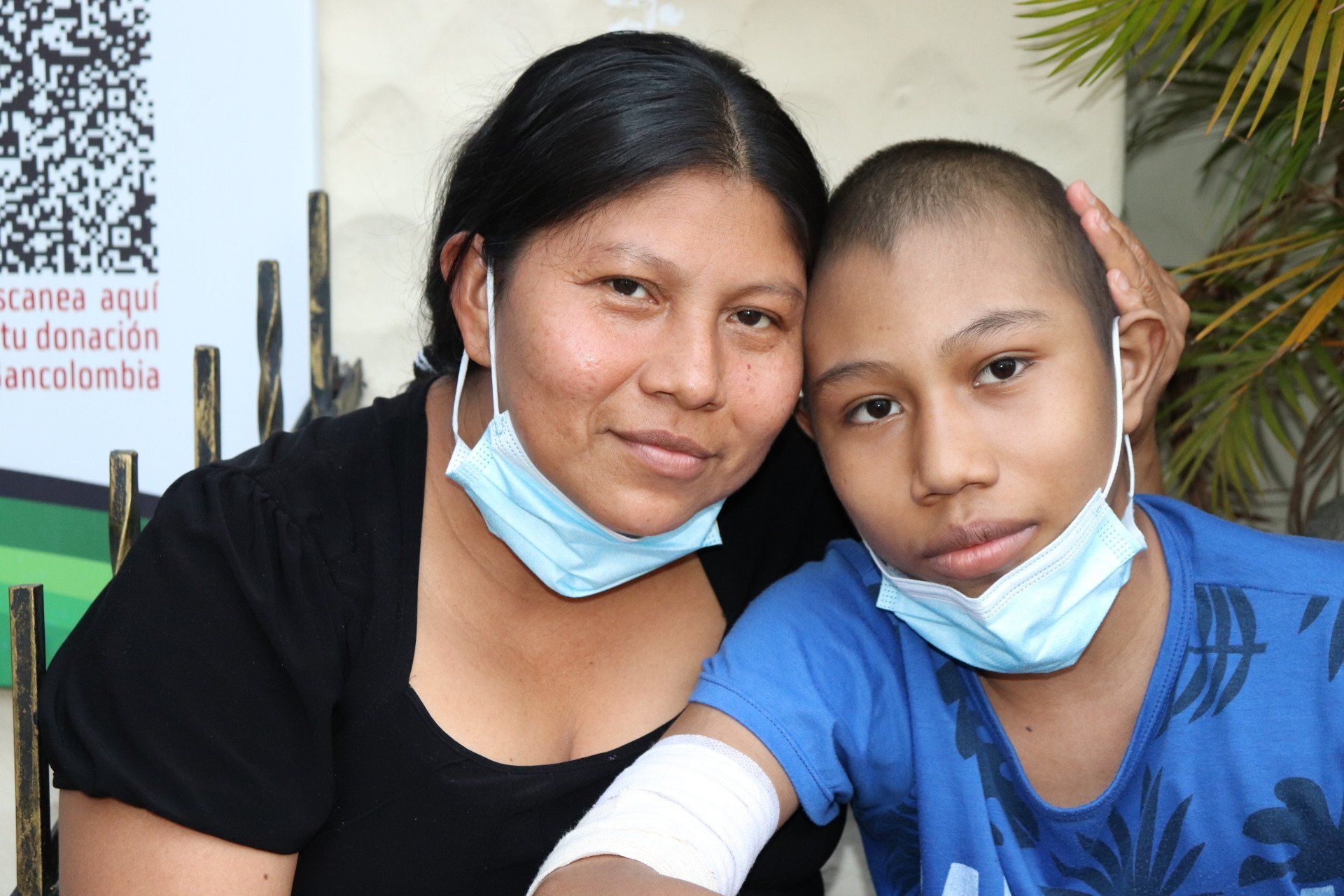 Mujer con niño, ambos con mascarillas. El niño tiene el brazo vendado y la cabeza rapada