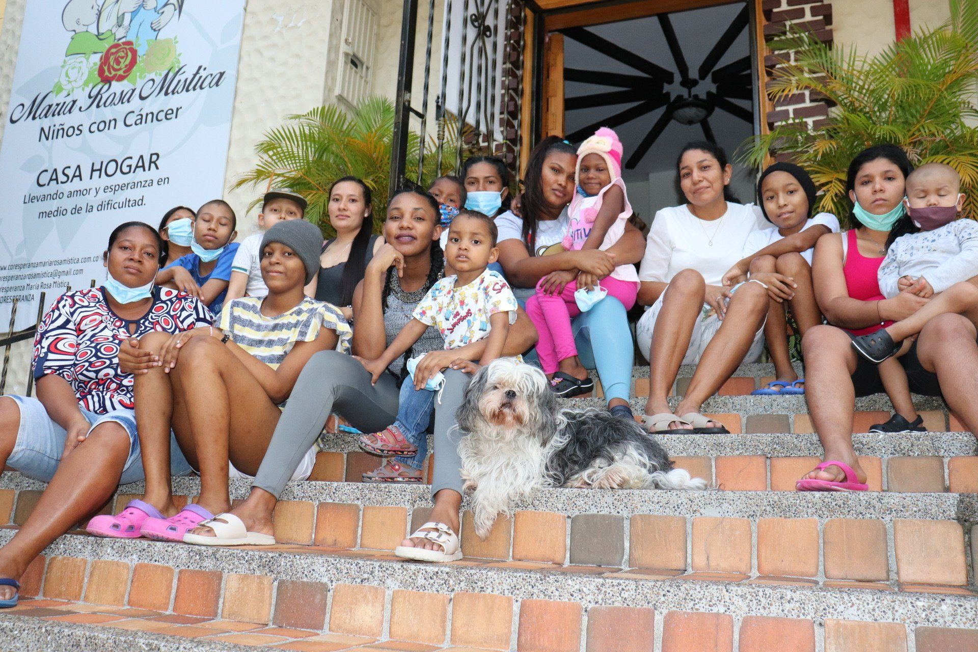 Grupo de personas, incluidos niños, sentados en las escaleras afuera de un edificio