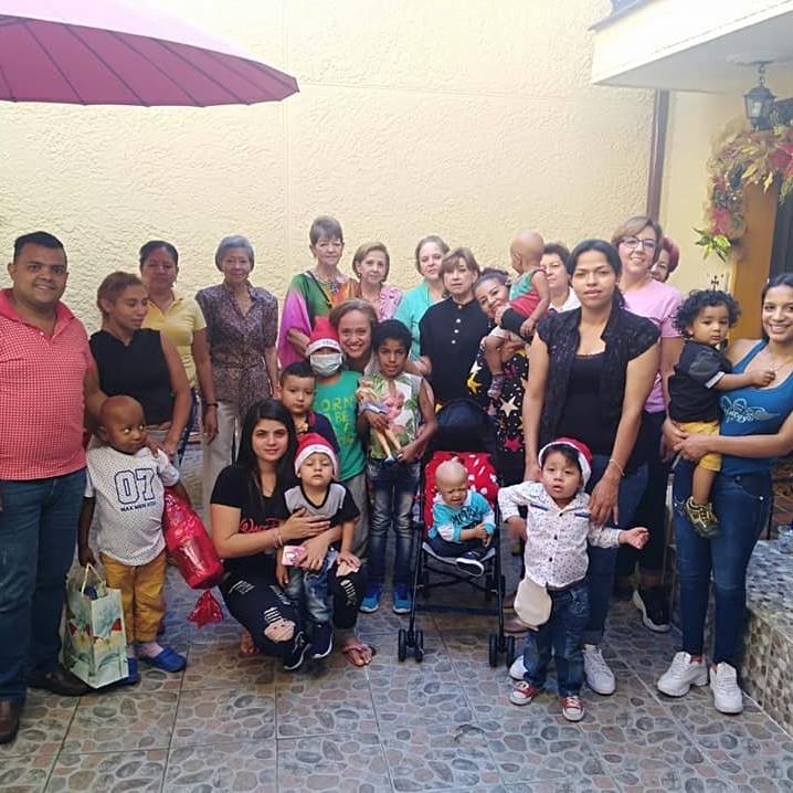 Grupo de personas y niños posando al aire libre, algunos sosteniendo niños, con sonrisas.