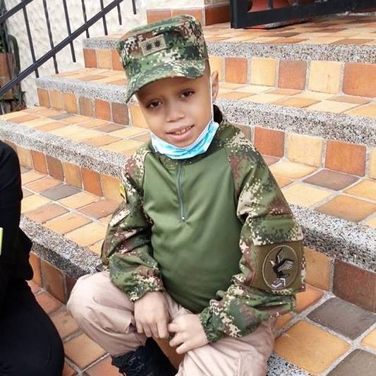 Niño con uniforme de camuflaje y sombrero, sentado en los escalones.