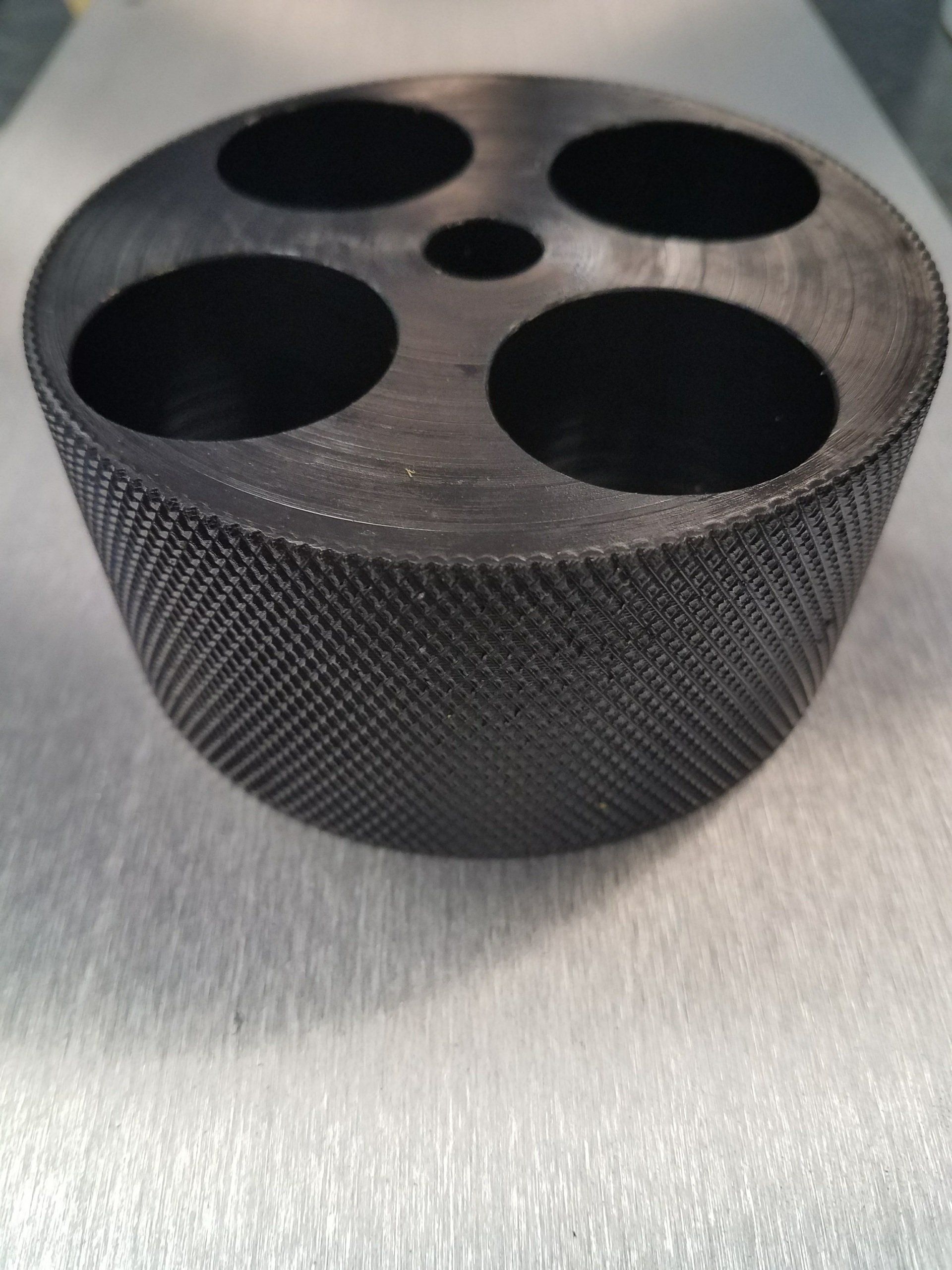 A black bowl with four holes in it is sitting on a table.