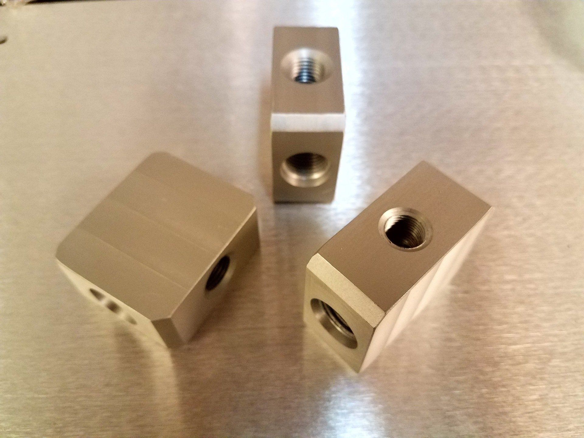 Three metal blocks with holes in them are sitting on a metal surface