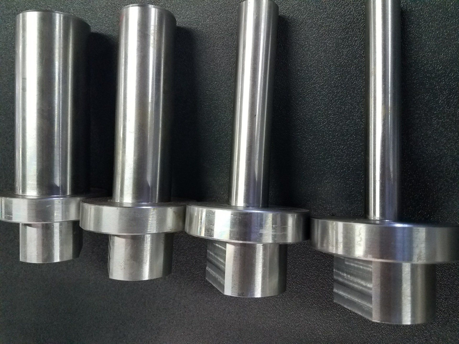Four stainless steel rods are lined up on a black surface