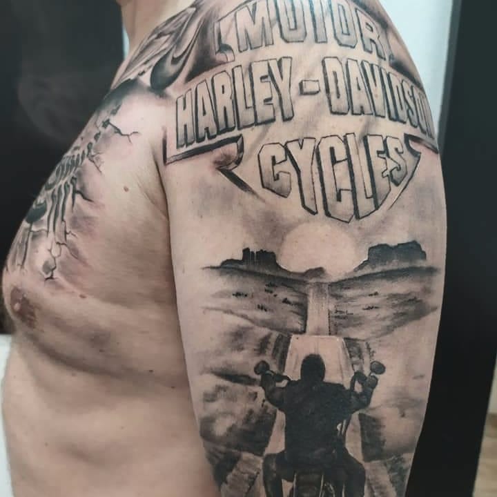 Armtattoo mit dem Harley-Davidson Cycles-Logo und der Silhouette eines Bikers auf einer Straße unter bewölktem Himmel