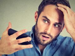 A man is combing his hair with a comb on a blue background.