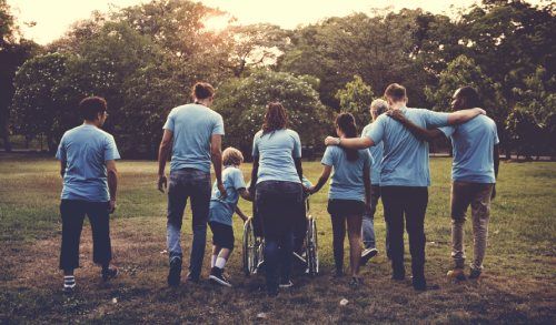 Un gruppo di persone con magliette blu cammina in un parco, alcune abbracciate, una su una sedia a rotelle.