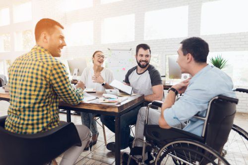 Un gruppo di persone sorridenti attorno a un tavolo in un ufficio, una persona usa una sedia a rotelle.