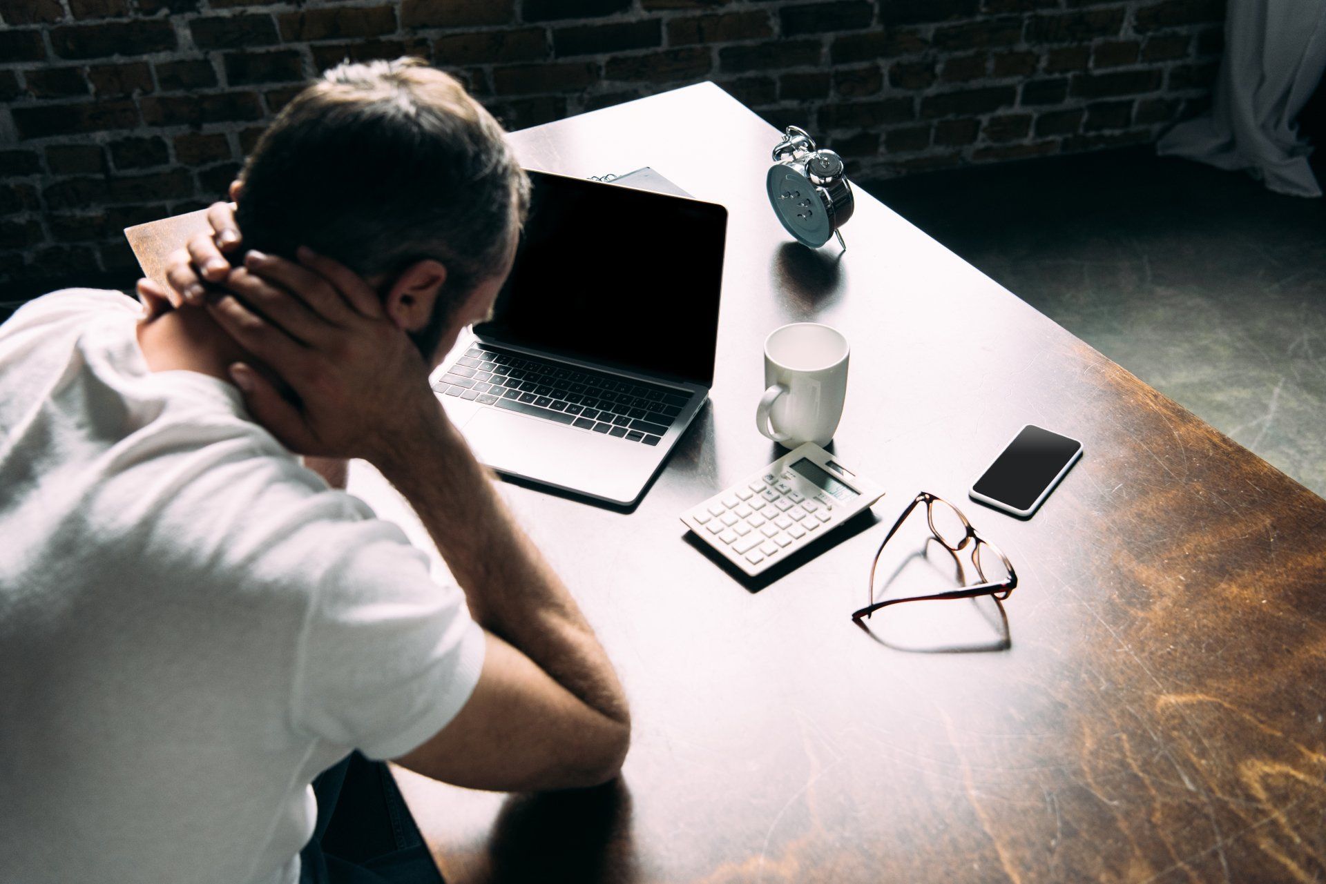 A man is sitting at a desk with a laptop and holding his neck.