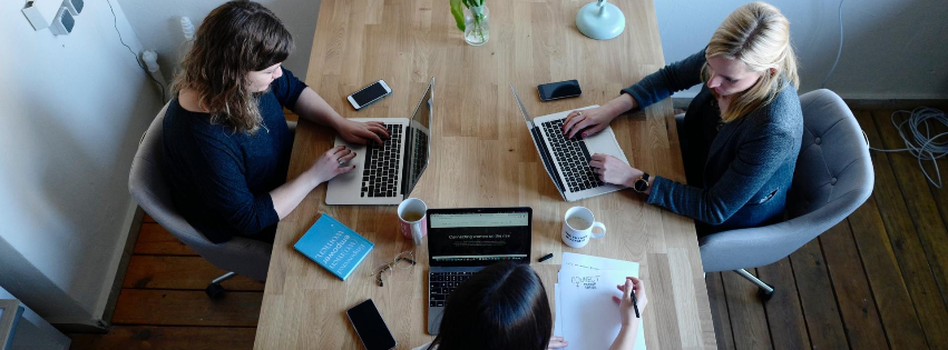 Three women are sitting at a table with laptops.