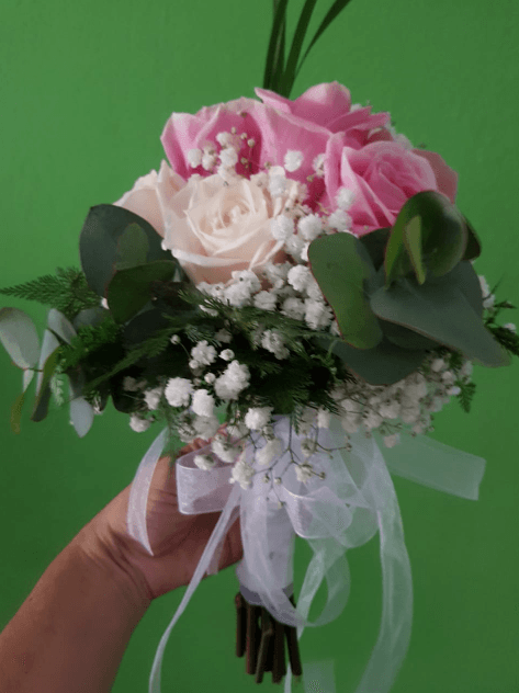 Una persona sostiene un ramo de rosas rosadas y flores de bebé.