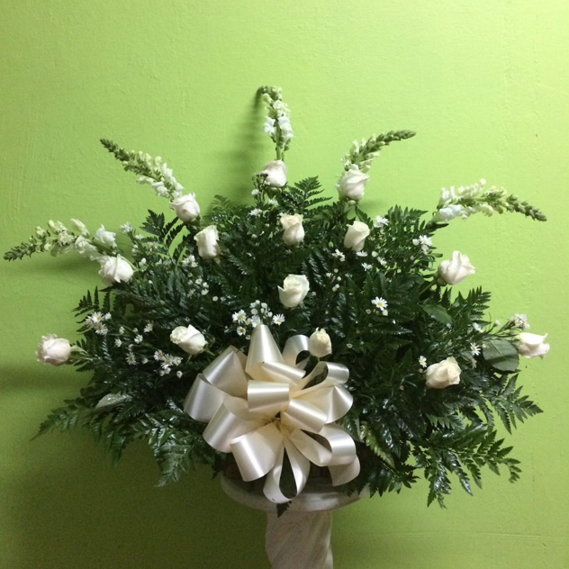 Un jarrón lleno de flores blancas y vegetación con un lazo blanco.