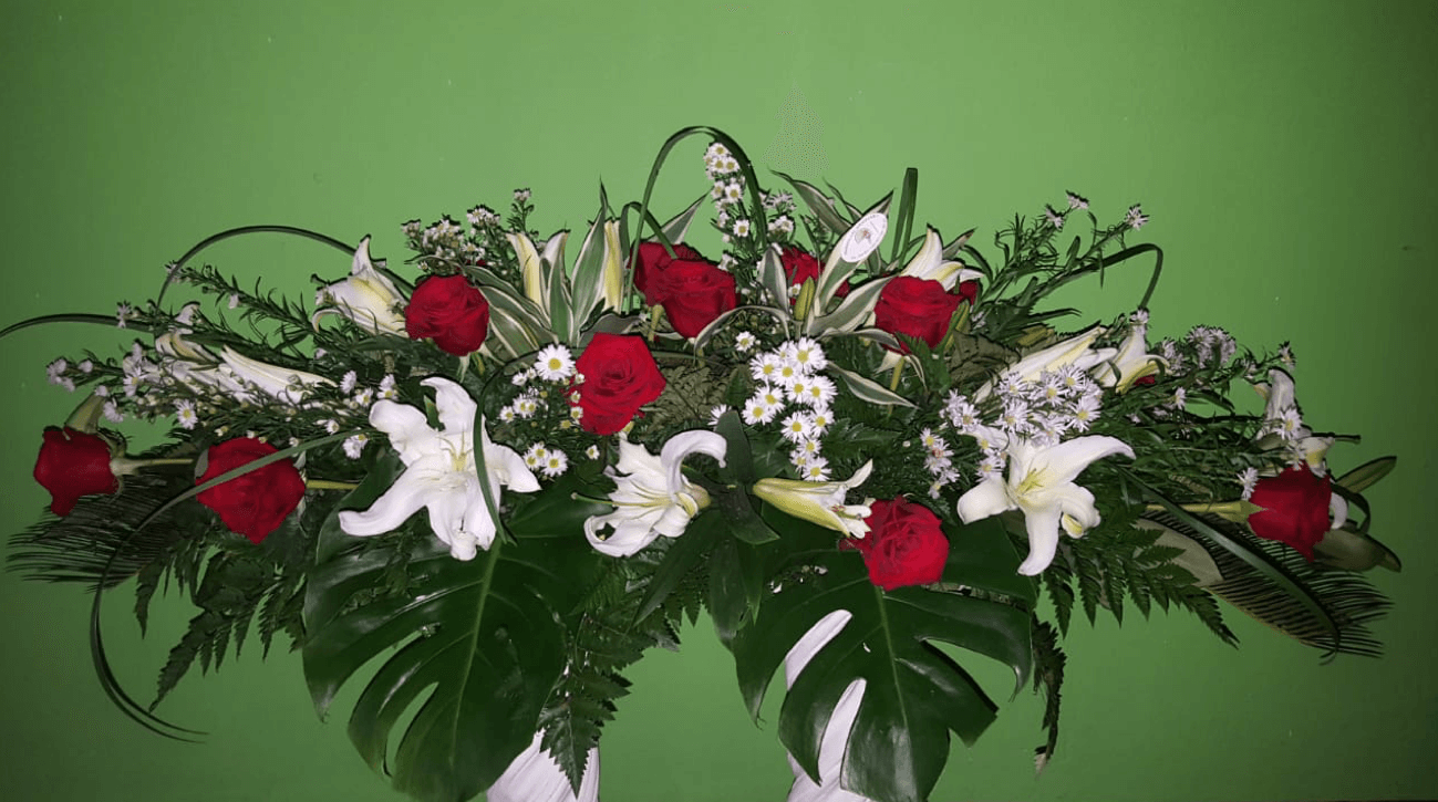 Un jarrón lleno de rosas rojas y lirios blancos sobre un fondo verde.