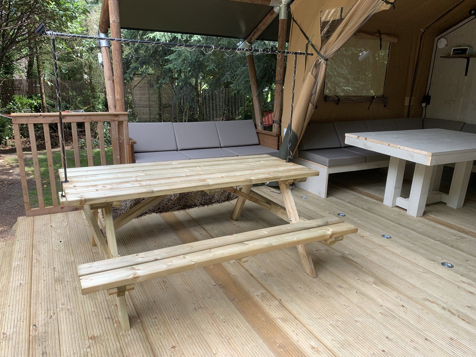 Een houten picknicktafel staat op een houten terras voor een tent.