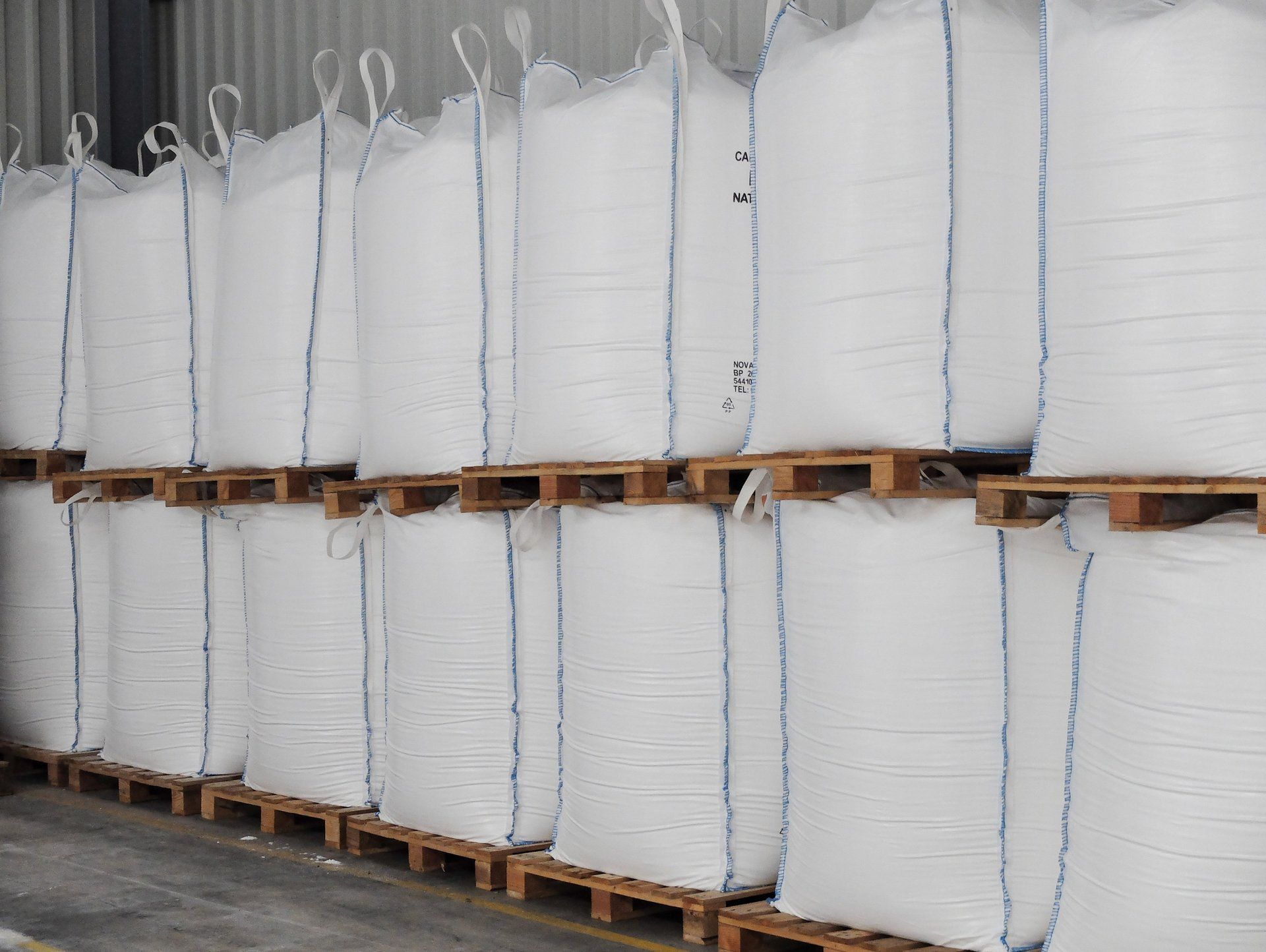 A lot of white bags are stacked on top of each other on wooden pallets.