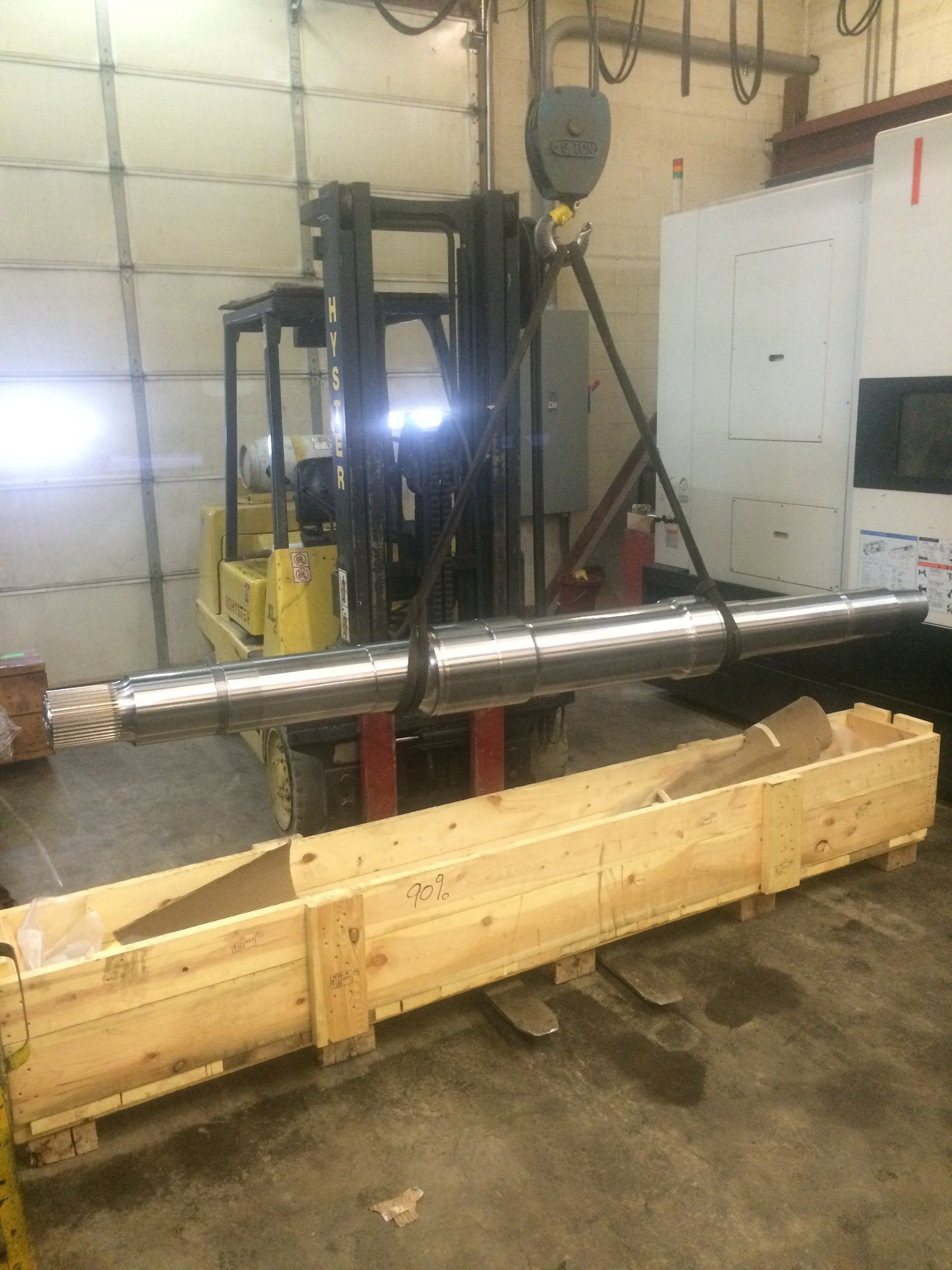 A forklift is carrying a large piece of metal in a wooden box