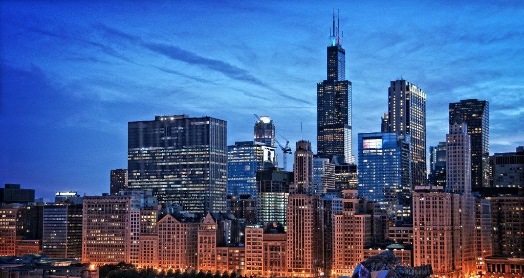 City skyline with tall buildings illuminated at dusk under a blue sky.