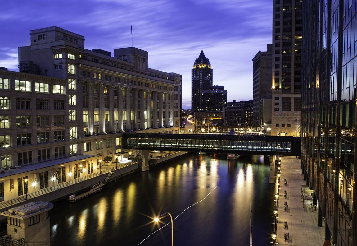 City buildings with a skywalk over a river at dusk.