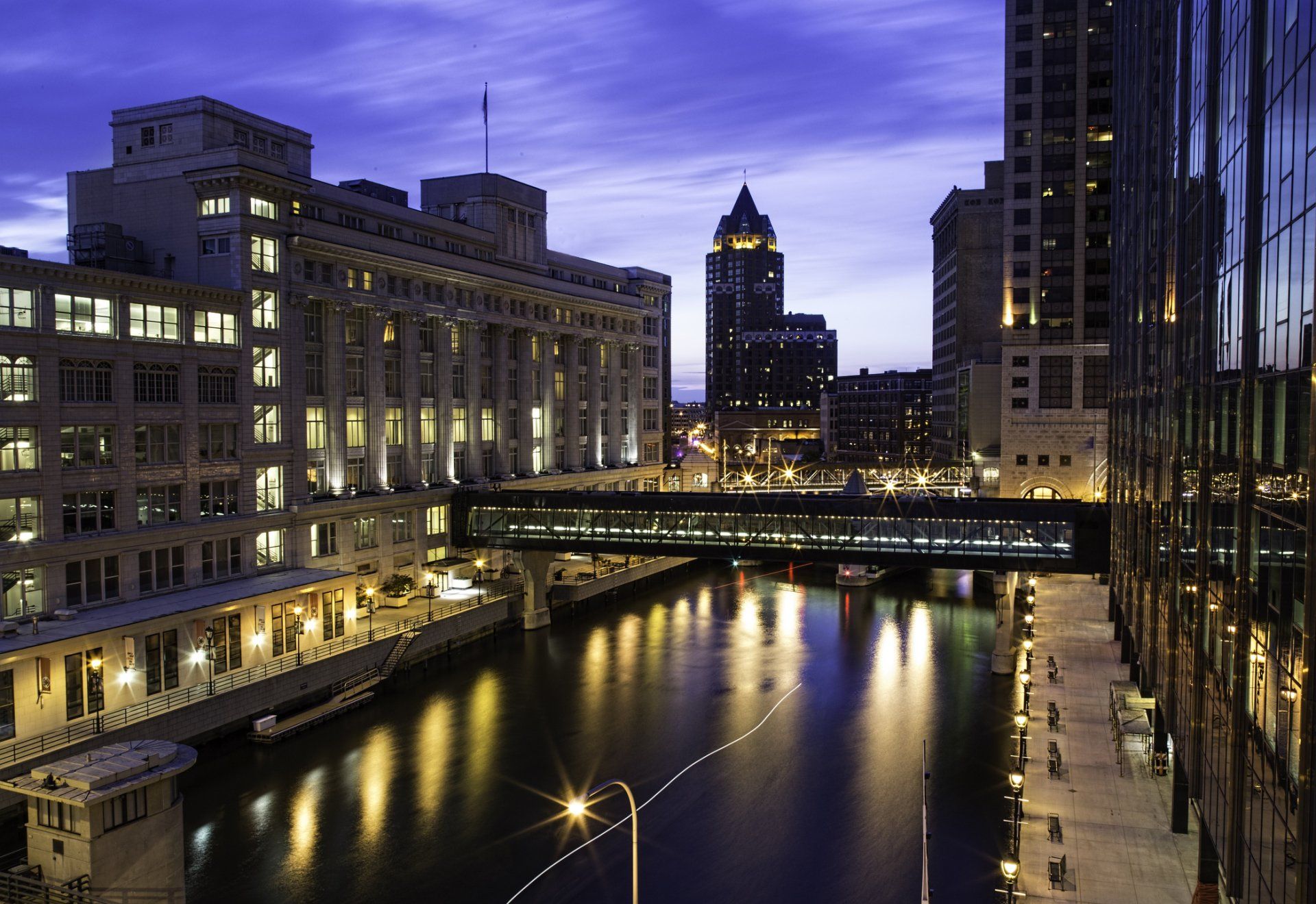 City buildings with a skywalk over a river at dusk.