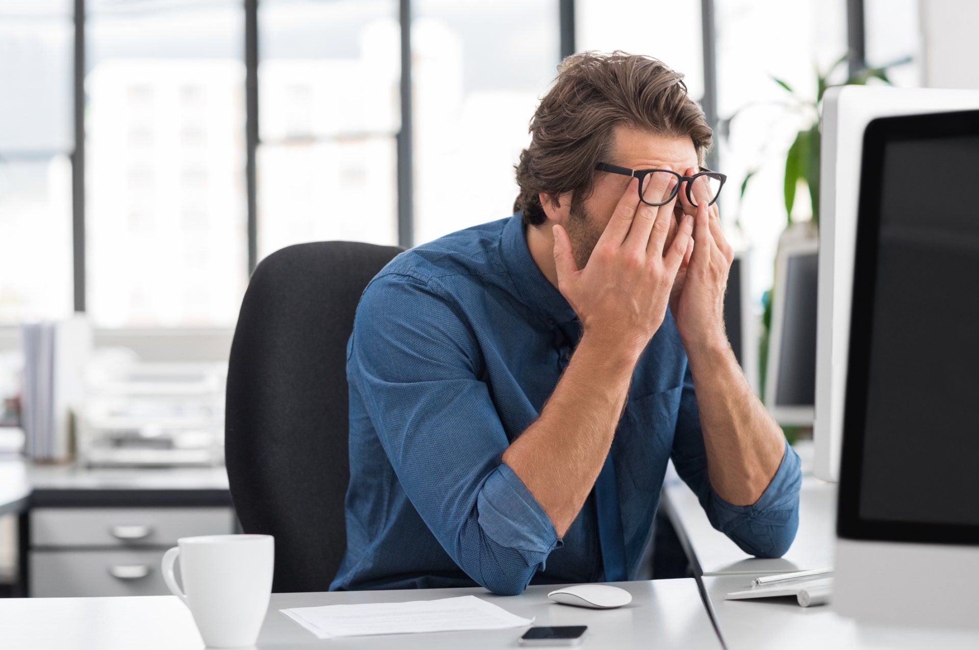 Person sitting at a desk with hands on head near a computer monitor.