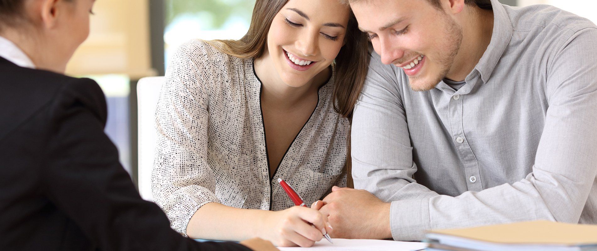Couple reviewing and signing documents with a professional at a desk.
