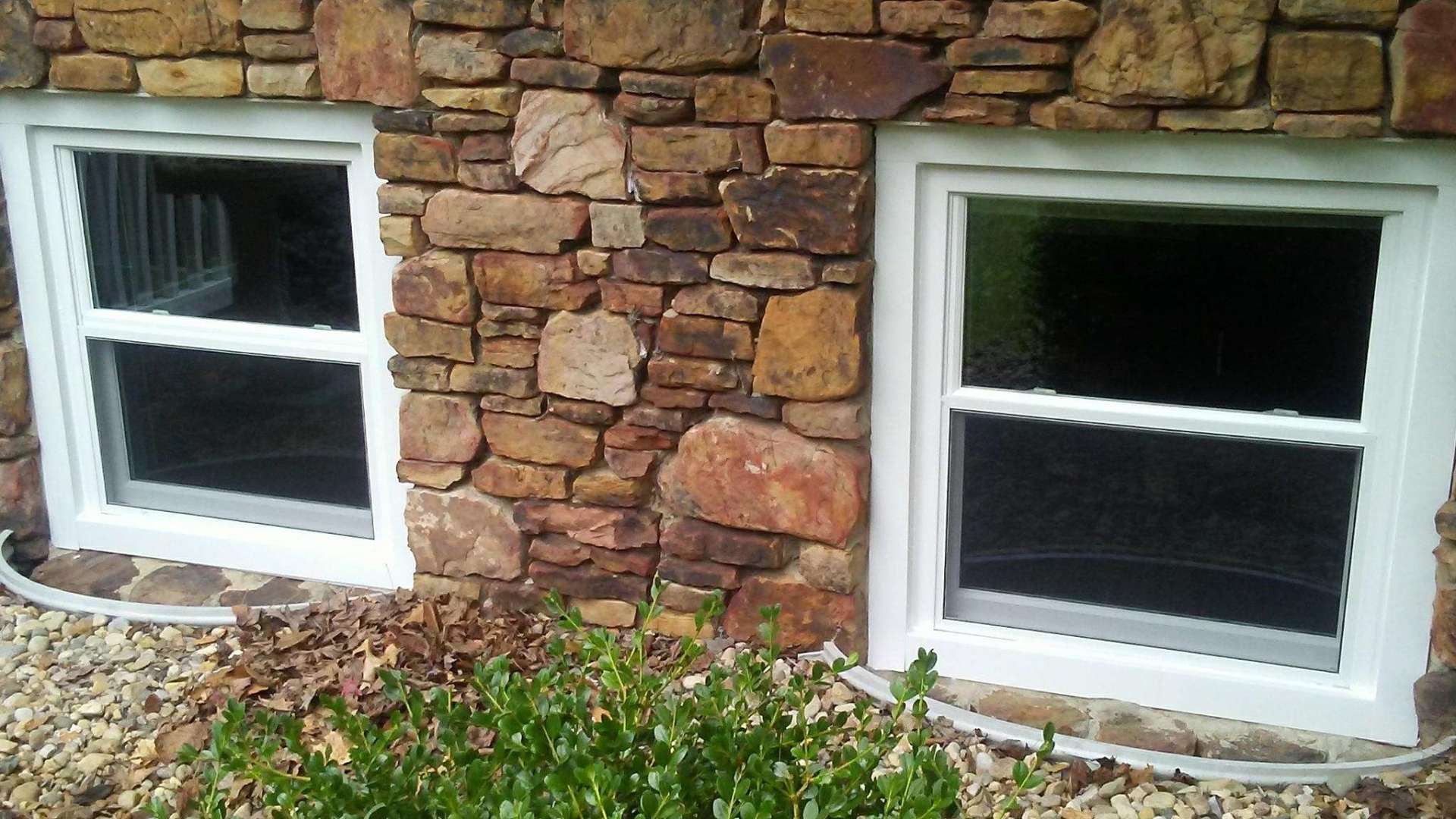 There are two windows on the side of a stone building.