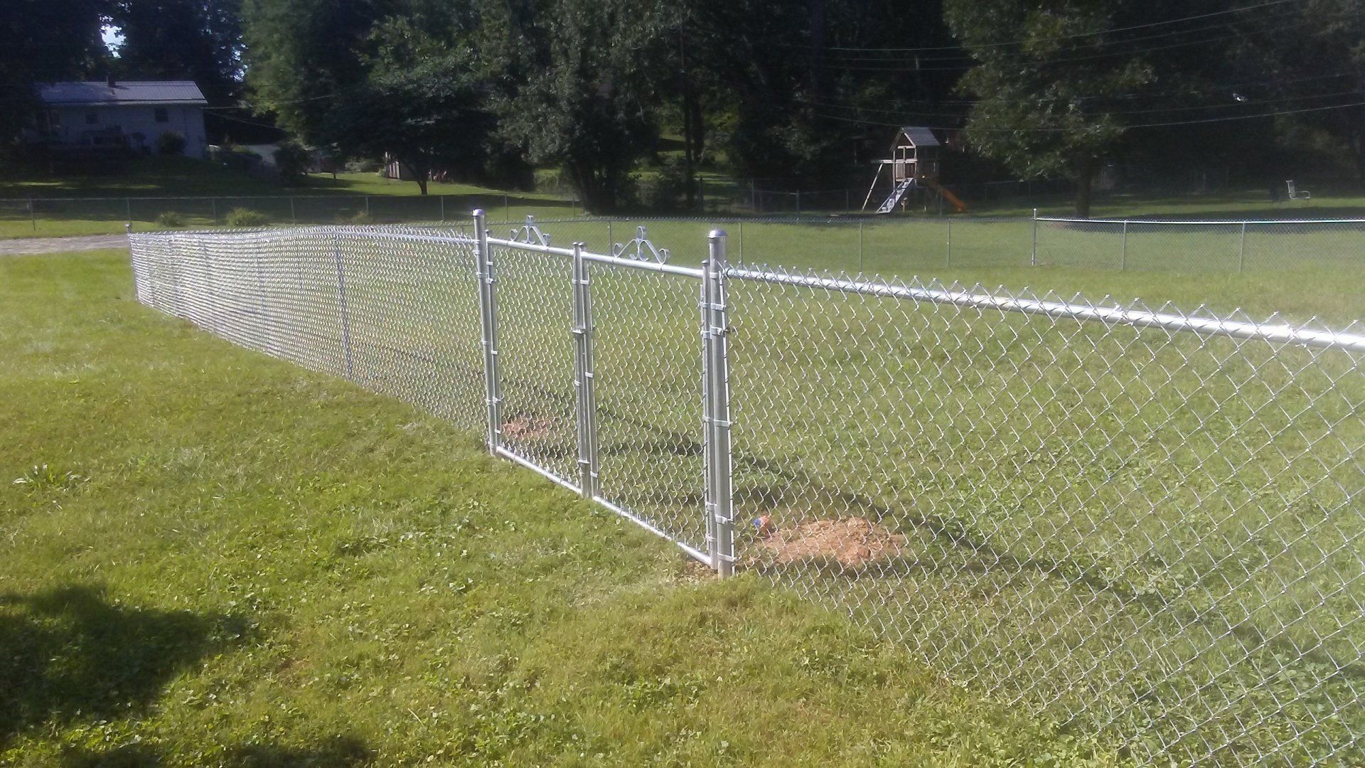 A chain link fence is in the middle of a grassy field.