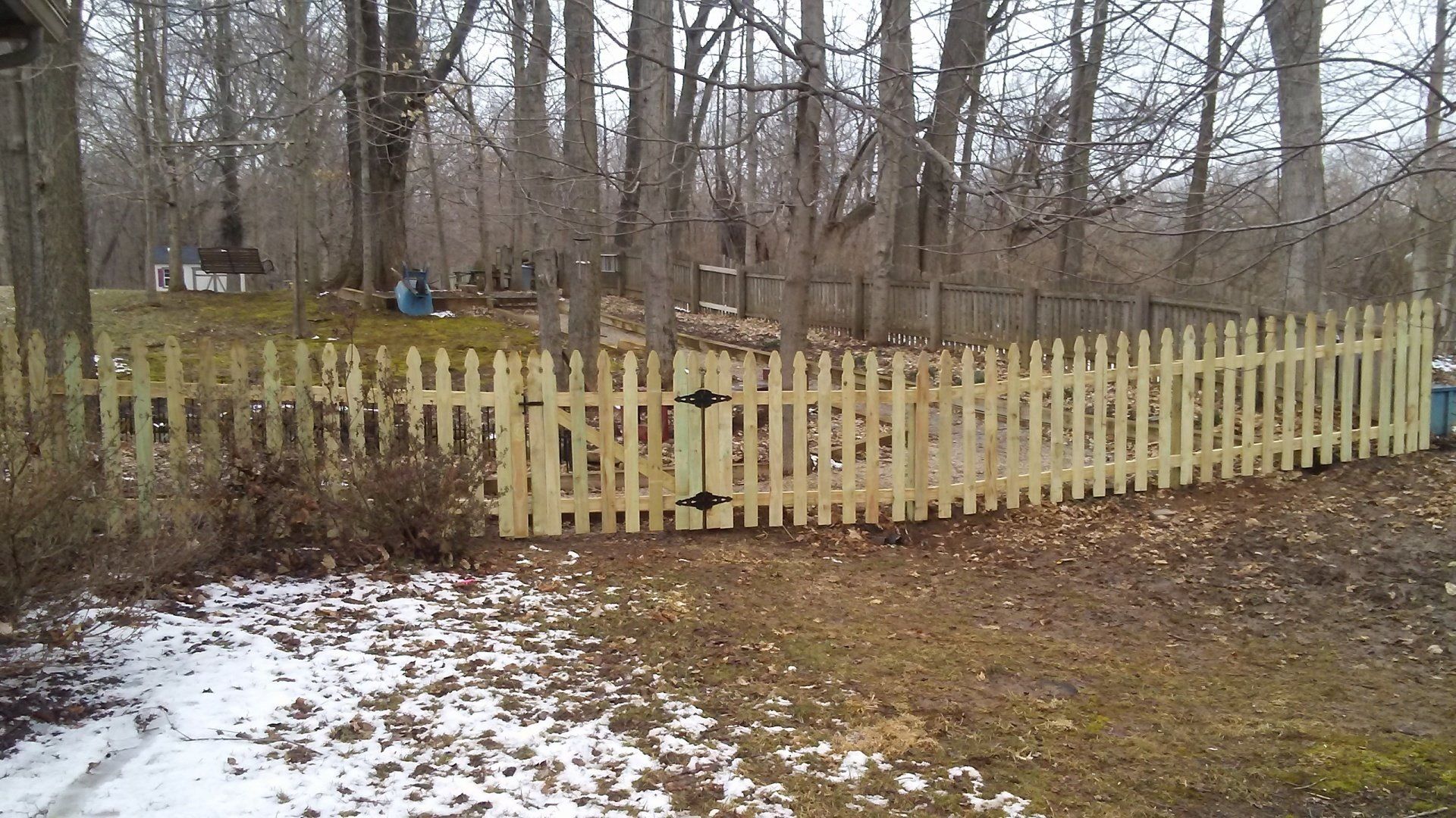 A wooden picket fence is surrounded by snow and trees.