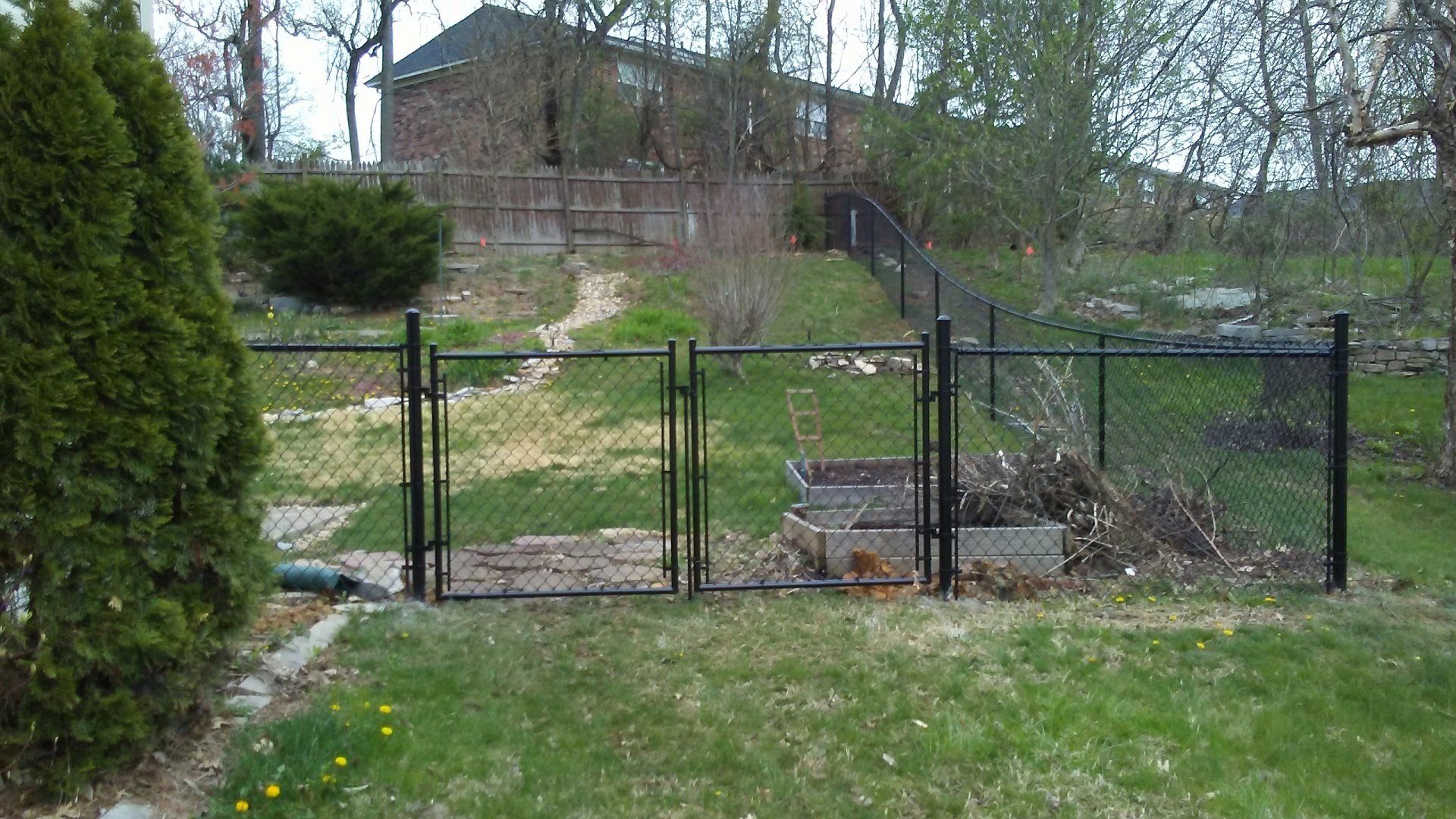 A chain link fence with a gate in the backyard of a house.