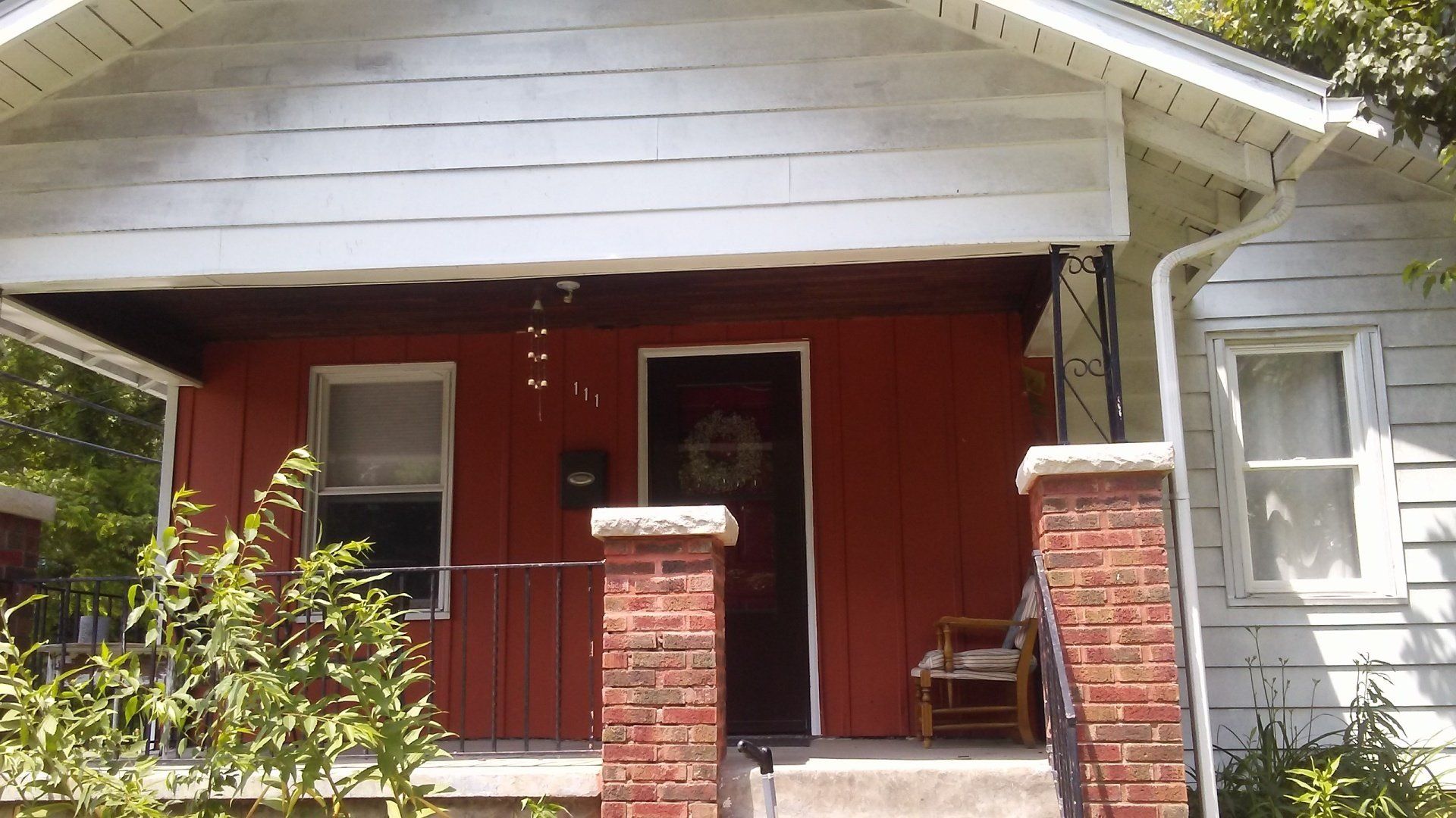 A white house with red siding and a brick porch