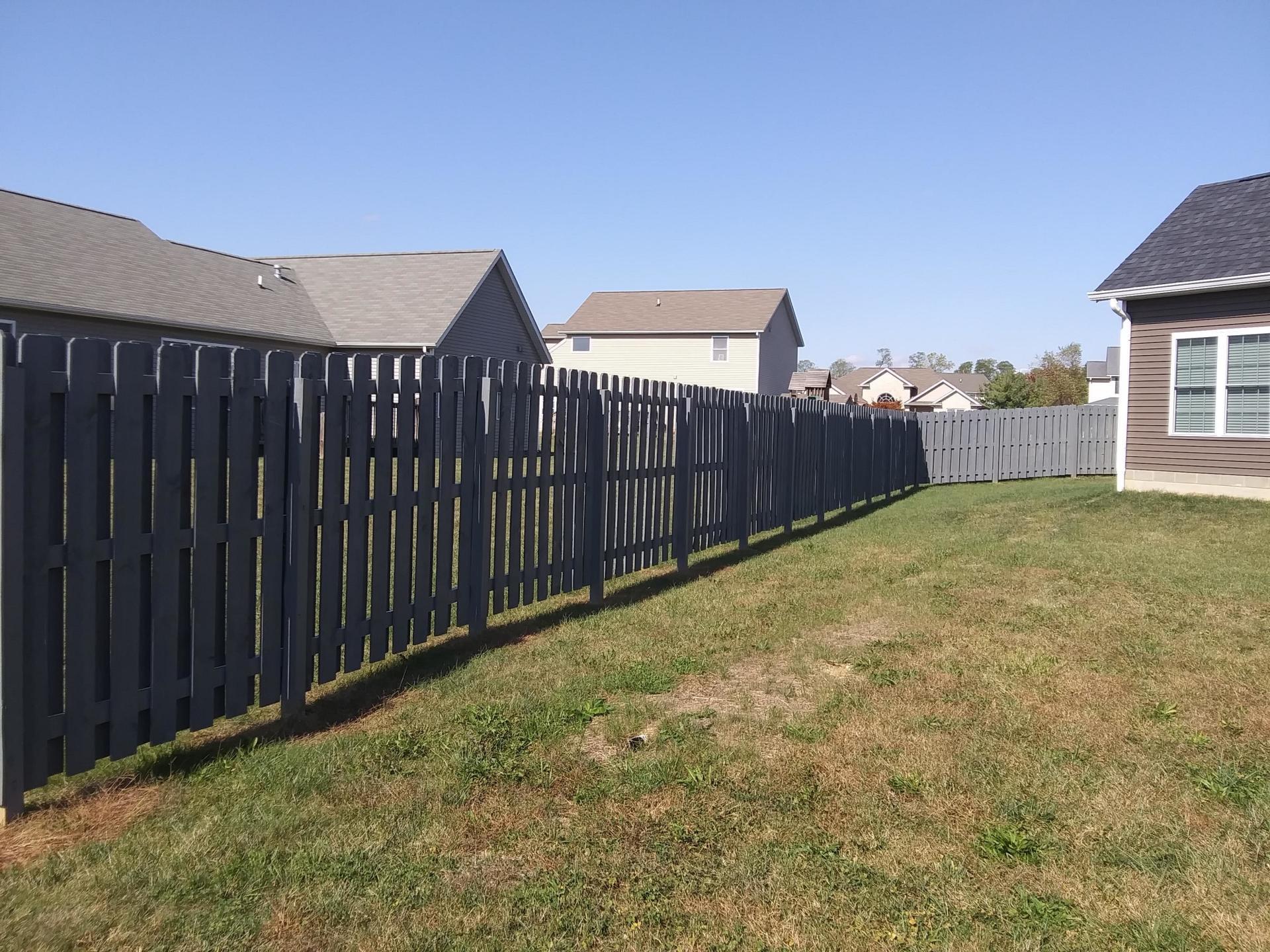 A wooden fence surrounds a lush green yard in front of a house.
