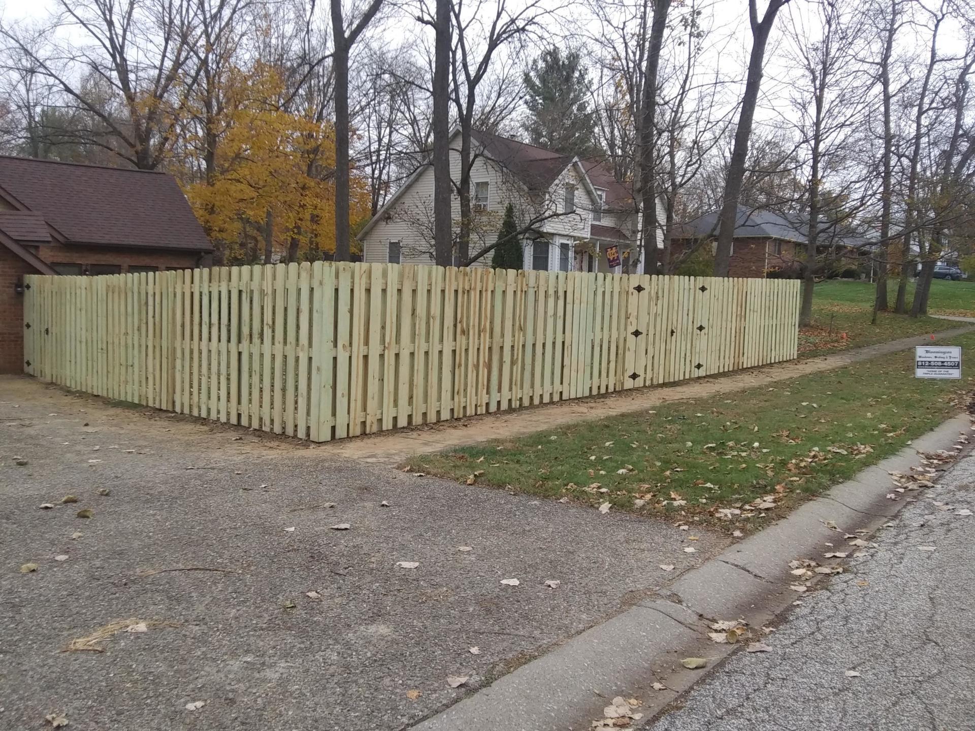 A wooden picket fence surrounds a yard in a residential neighborhood.