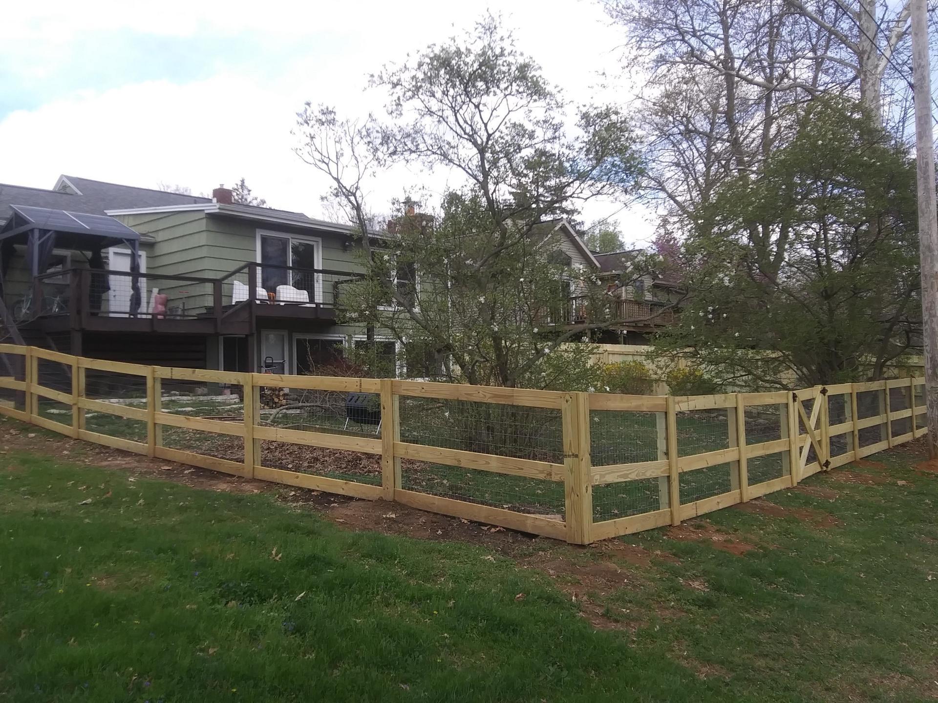 A wooden fence surrounds a lush green yard in front of a house.