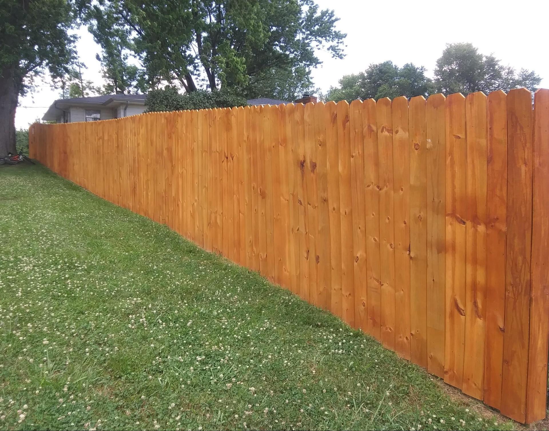 A long wooden fence surrounds a lush green yard.