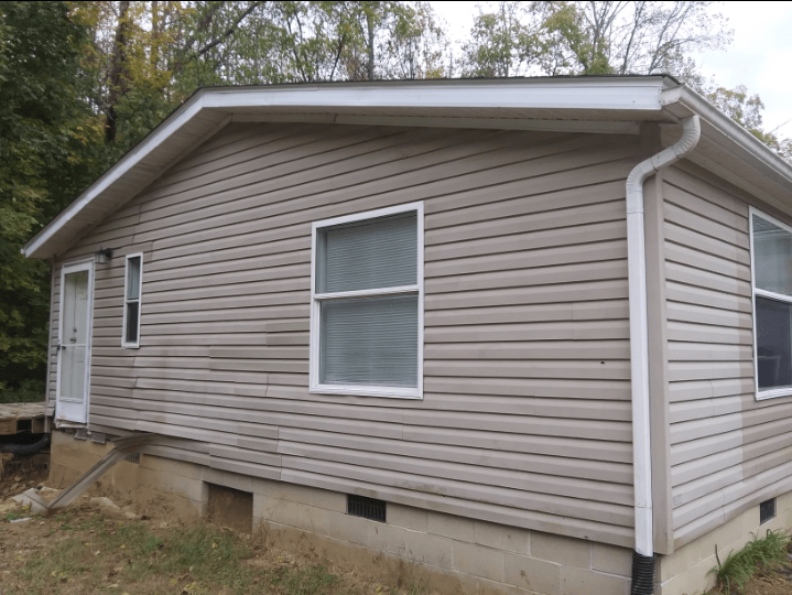 A small house with a tan siding and white windows