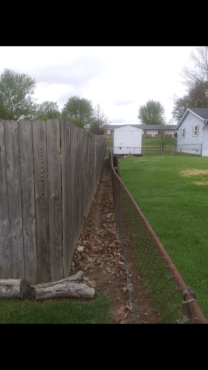 A wooden fence surrounds a yard with a white house in the background.