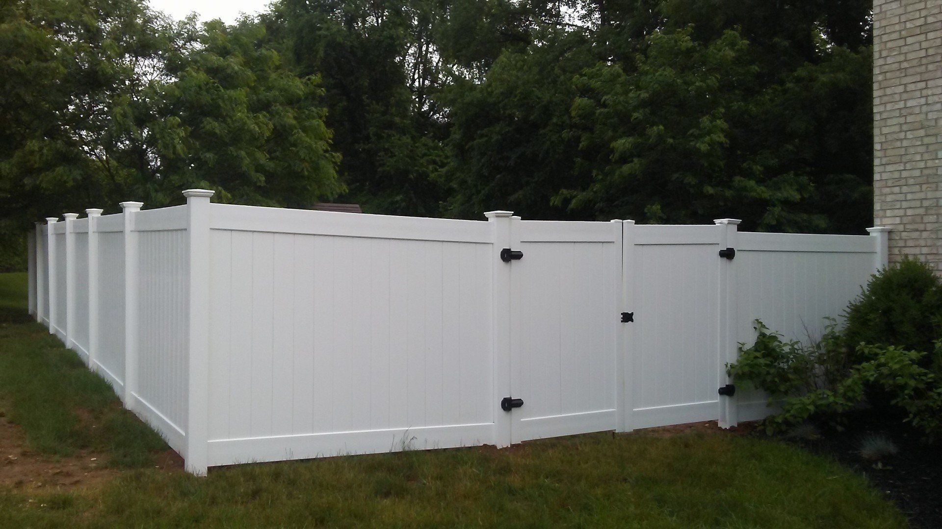 A white vinyl fence with a gate in the backyard of a house.