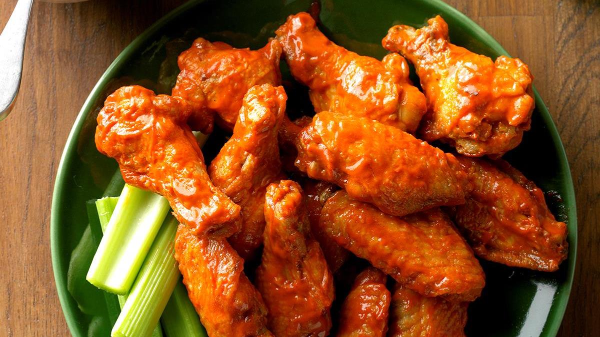 Buffalo wings on a green plate with celery sticks; wooden table.