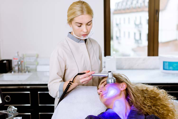 Beautician-doctor-doing-blue-led-light-therapy-to-female-customer-in-beauty-salon