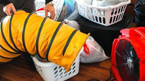 Person using an accordion-style yellow hose to direct air from a red fan near laundry baskets.