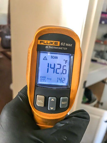 Hand holding an orange Fluke 62 MAX infrared thermometer displaying a temperature of 142.6°F.