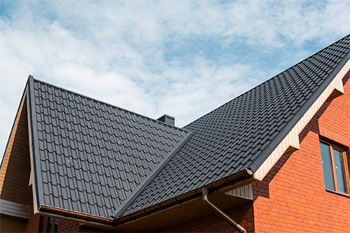 A brick house with a black roof and a blue sky in the background.